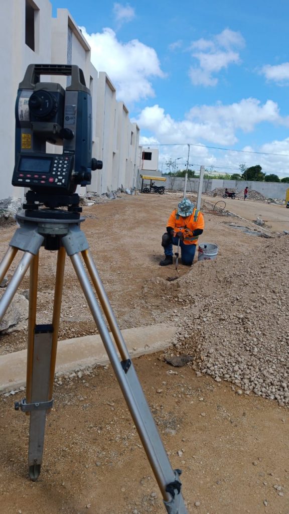 Estación total topográfica de alta precisión en primer plano durante un levantamiento en una obra residencial, con un especialista trabajando al fondo.